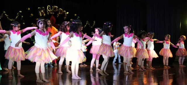 Young students in pink and yellow costumes performing a dance on stage