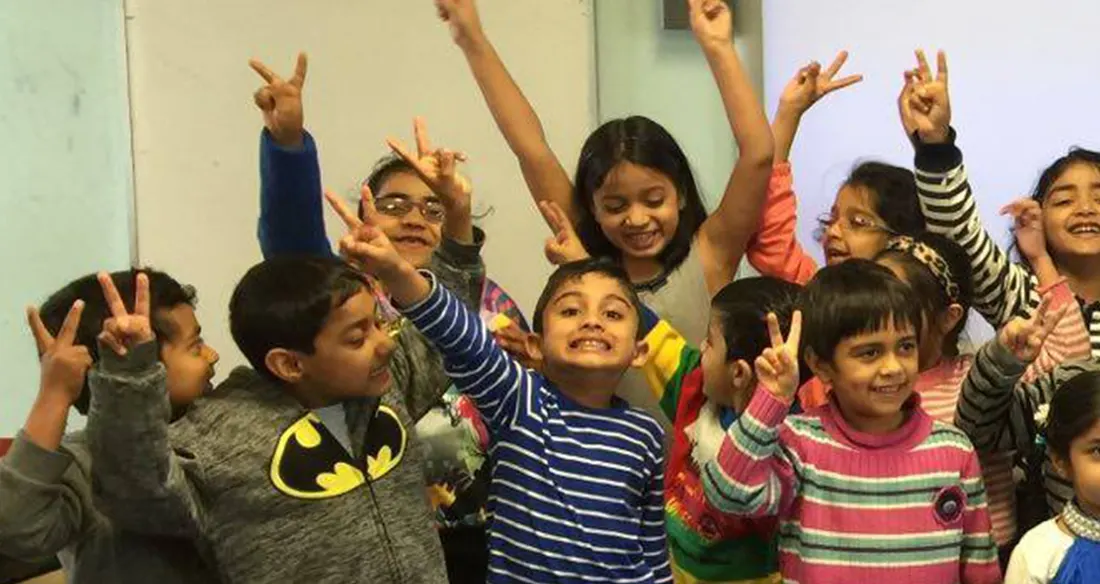 A classroom of smiling South Asian Hindi School students waving at the camera